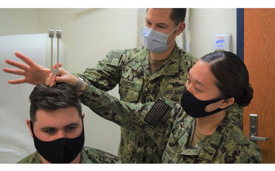 Navy Lt. Jeffrey Osborn, physician assistant (PA) assigned to Navy Readiness and Training Command Bremerton’s Branch Health Clinic Bangor demonstrates to Navy Hospitalmen Wendy Dang (right) and Nicholas Gevedon (seated) the Rinne and Weber test(s) routinely used to evaluate hearing loss. Osborn attests that “the single best part of his job is training and working with corpsmen. (Photo by Douglas Stutz, NHB/NMRTC Bremerton.)