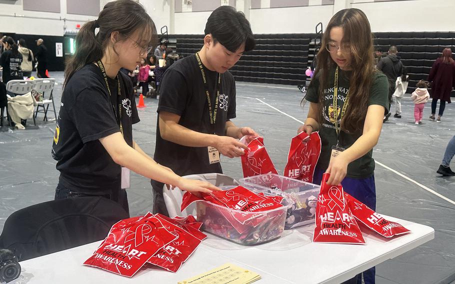 Minseo Harthausen, left, Mathew Huang, center, and Kayla Collins set up a Science Day welcome table in the gym at Humphreys High School at Camp Humphreys.