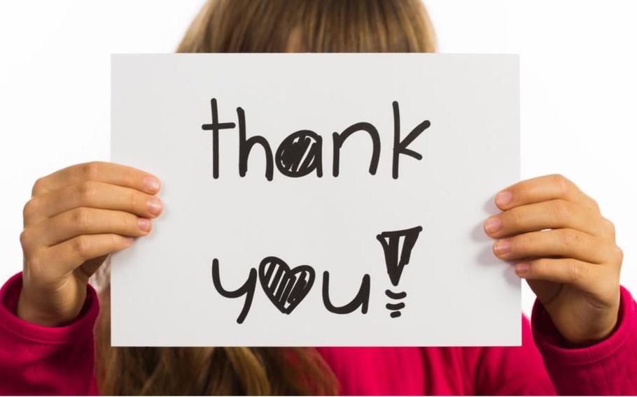 Studio shot of child holding a Thank You sign made of white paper with handwriting.