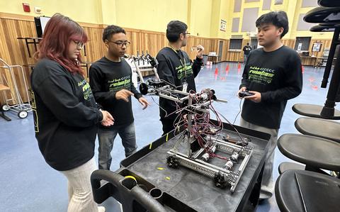 Photo Of Minseo Harthausen, left, Mathew Huang, center, and Kayla Collins set up a Science Day welcome table in the gym at Humphreys High School at Camp Humphreys.