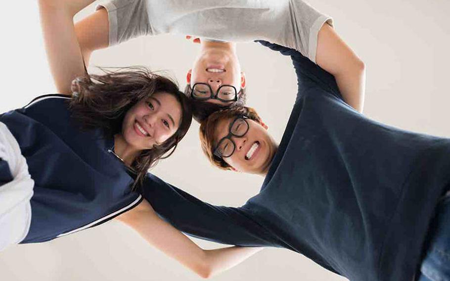 Hugging Asian friends standing in circle and smiling ta camera, view from below