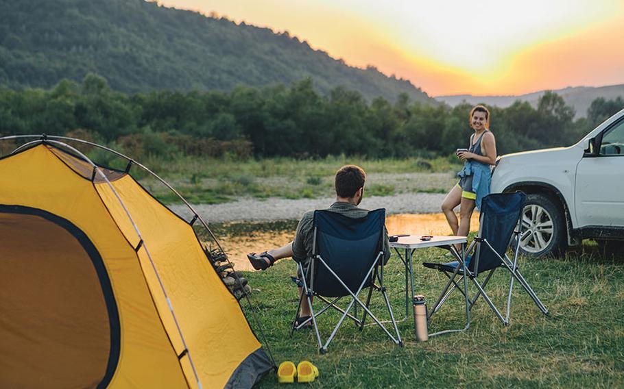 couple sitting in camp chairs looking at sunset above river in mountains.