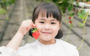 a young girl posing with a strawberry in a farm.