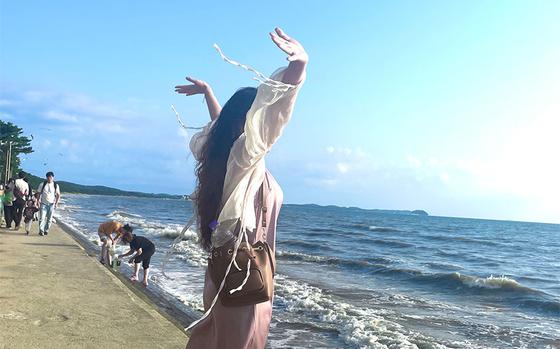 Hyemin is raising her hands on the beach.