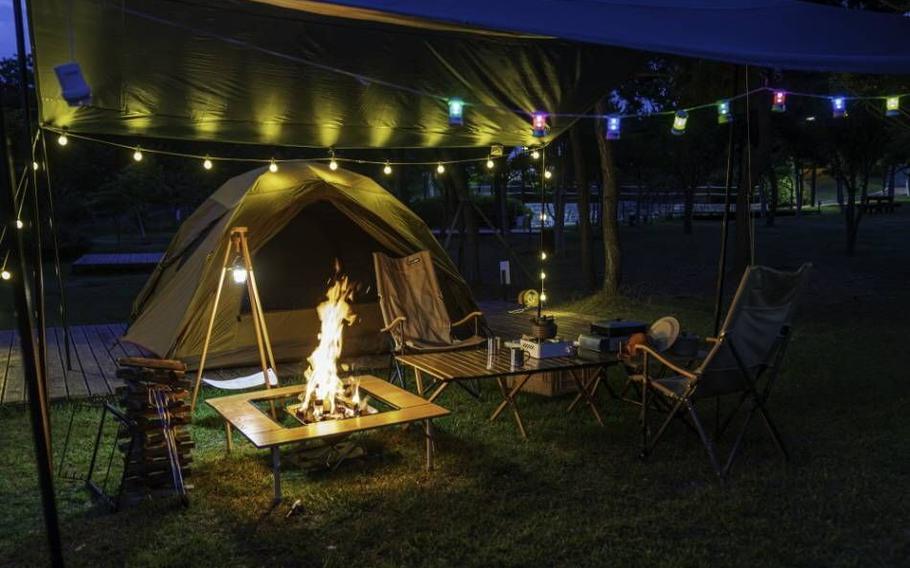 campfire, tent, table, and chairs can be seen.