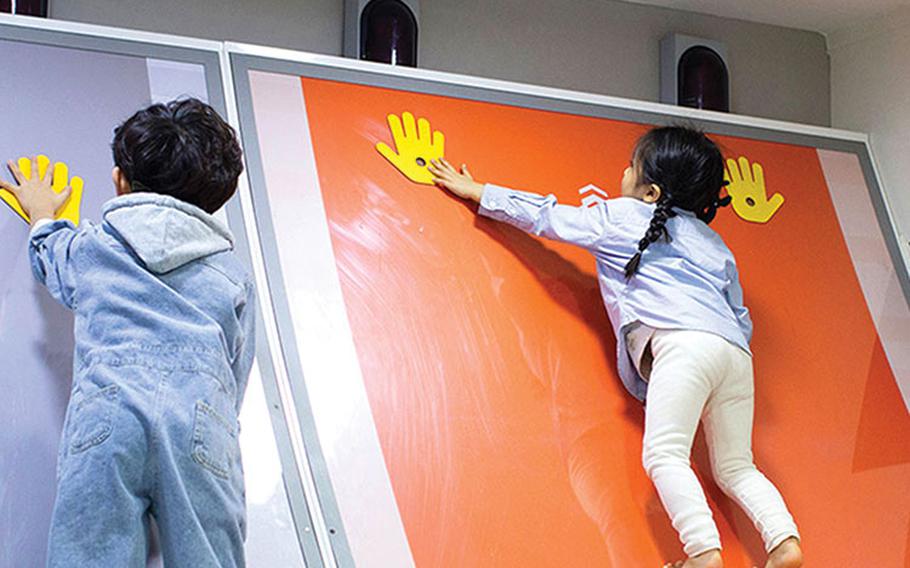 two kids enjoying a wall with printed hands’ shapes.