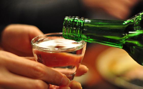 A person is accepting a bottle of soju.