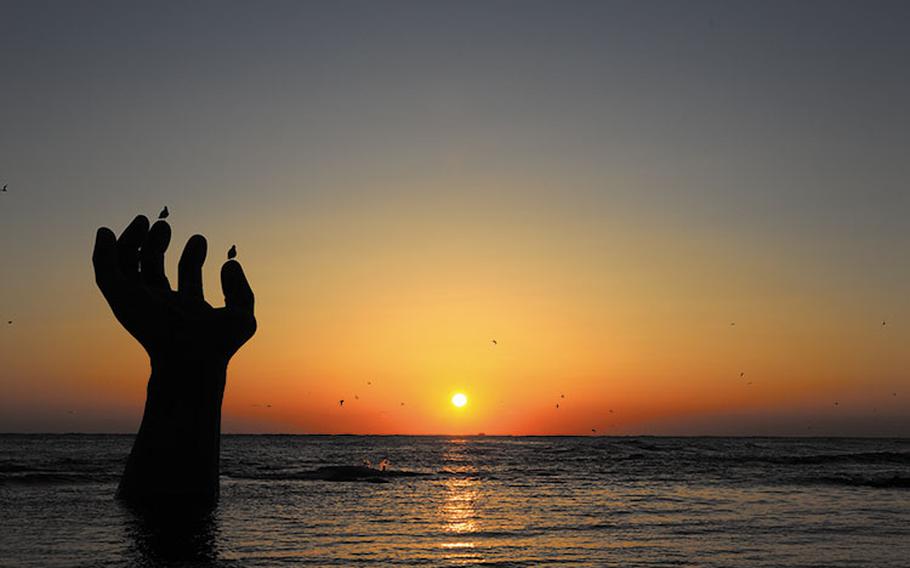 sunrise at Homigot Sunrise Square. a statue of a huge hand is on the beach.