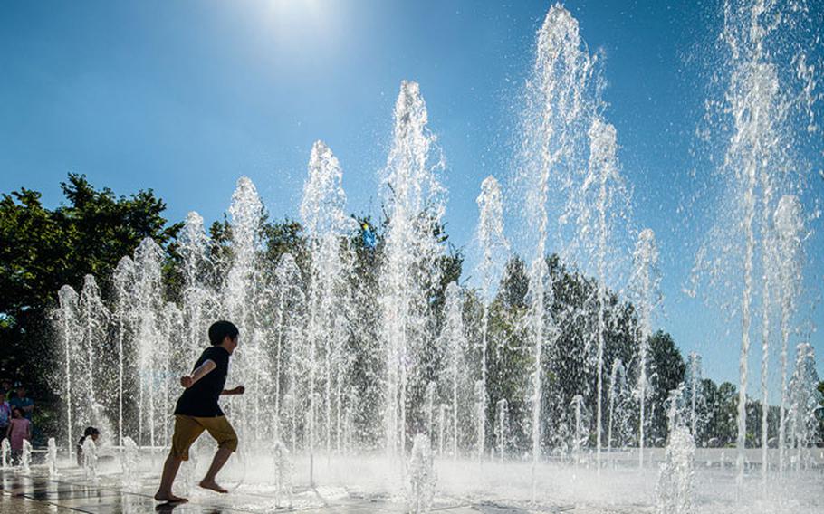 A boy is enjoying a fountain on a sunny day.