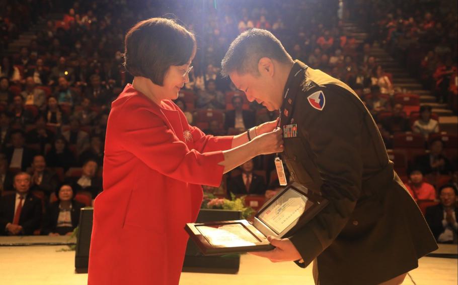 U.S. Army Col. Edward Cho receives an honorary citizenship award on the stage. There are many audience.