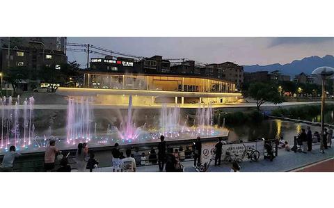 Photo Of Visitors are enjoying an illuminated fountain on the riverside in the evening.