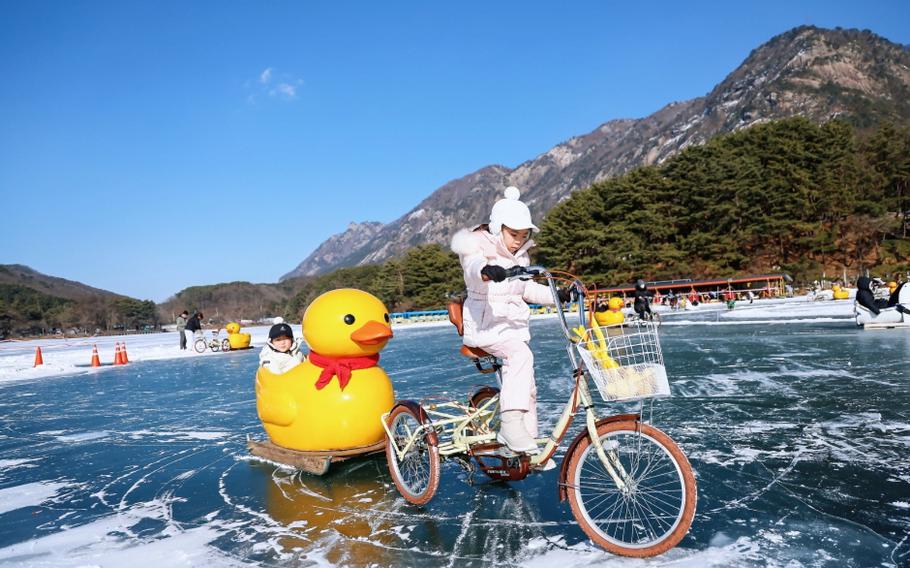 a girl riding a tricycle is pulling a sled with another girl on on the ice.