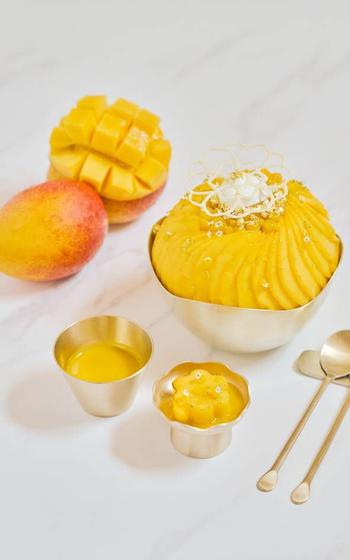 Mango bingsu, fork , and spoon are on the table.