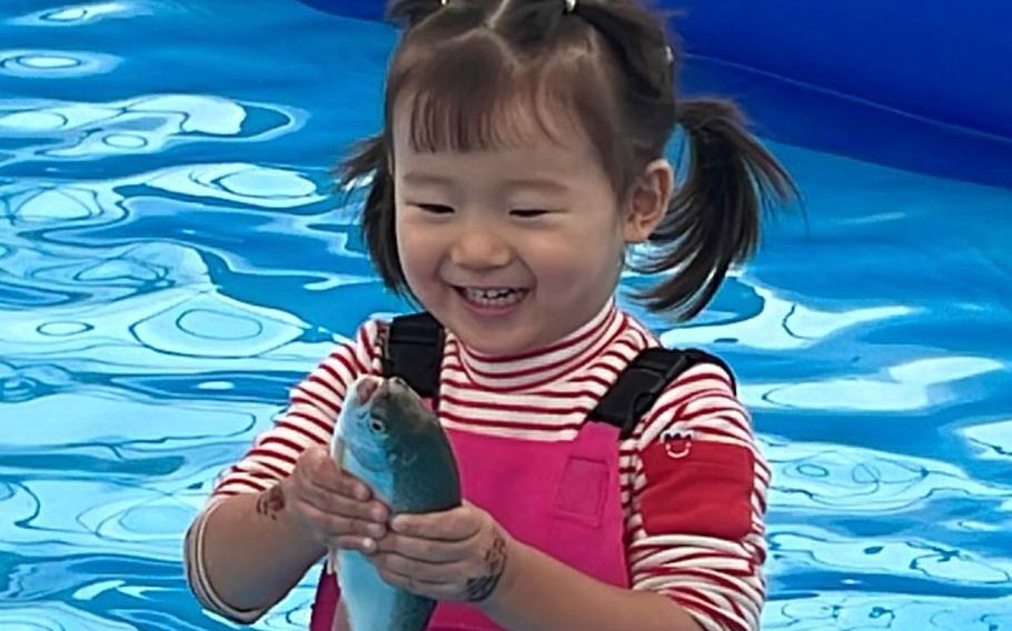 a girl smiling with a fish in her hand.