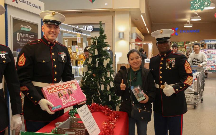 U.S. Marine Corps Sgt. Maj. Ismael Bamba and Staff Sgt. Jonathan Hemme poses for a photo alongside a civilian. A table and a Christmas tree are near them.