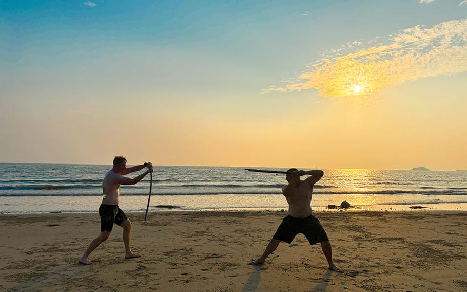 Two men are pretending to have a sword battle on the beach.