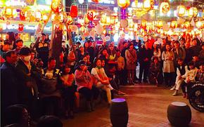 Many audience are watching something outside. there are many lanterns above them.