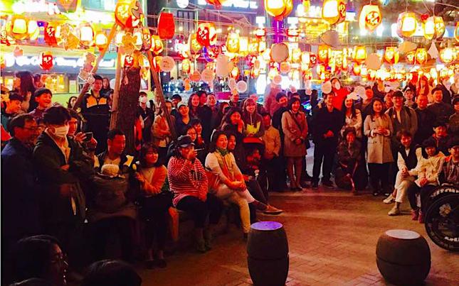 Many audience are watching something outside. there are many lanterns above them.