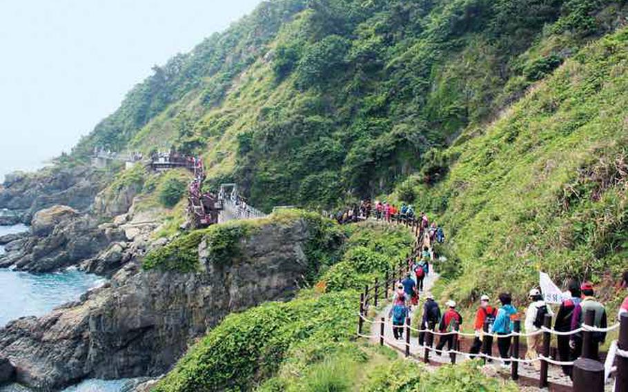 people are walking on the trail by the sea.