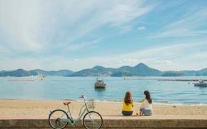 two women seating on the beach.