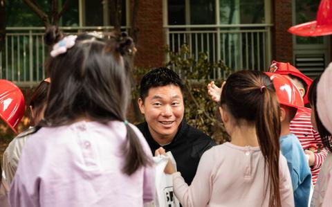 Photo Of Squatting down, Jiho Lee hands out information bags to Republic of Korea students.