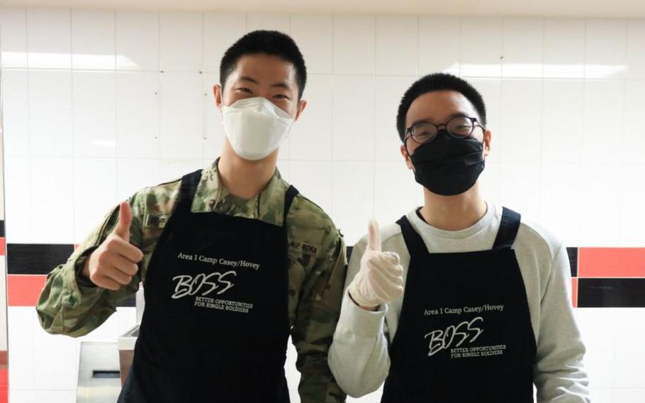 Korean Augmentation To the U.S. Army (KATUSA) Pfc. Joo Won Kim (left) and KATUSA Pfc. Ji Ho Yang, both assigned to U.S. Army Garrison Yongsan-Casey, pose for a commemorative photograph. The two wear aprons.