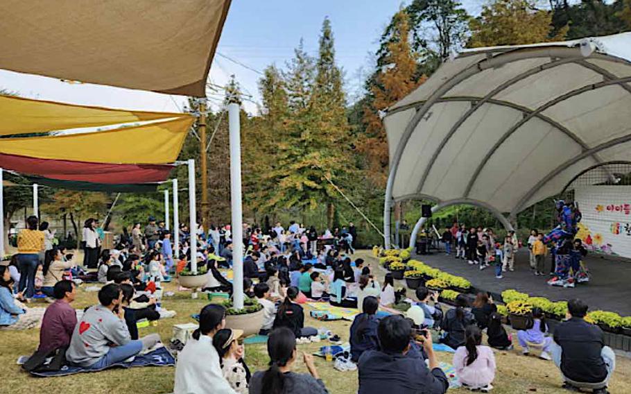 audience having seats on the lawn are enjoying a concert held at an outdoor stage.