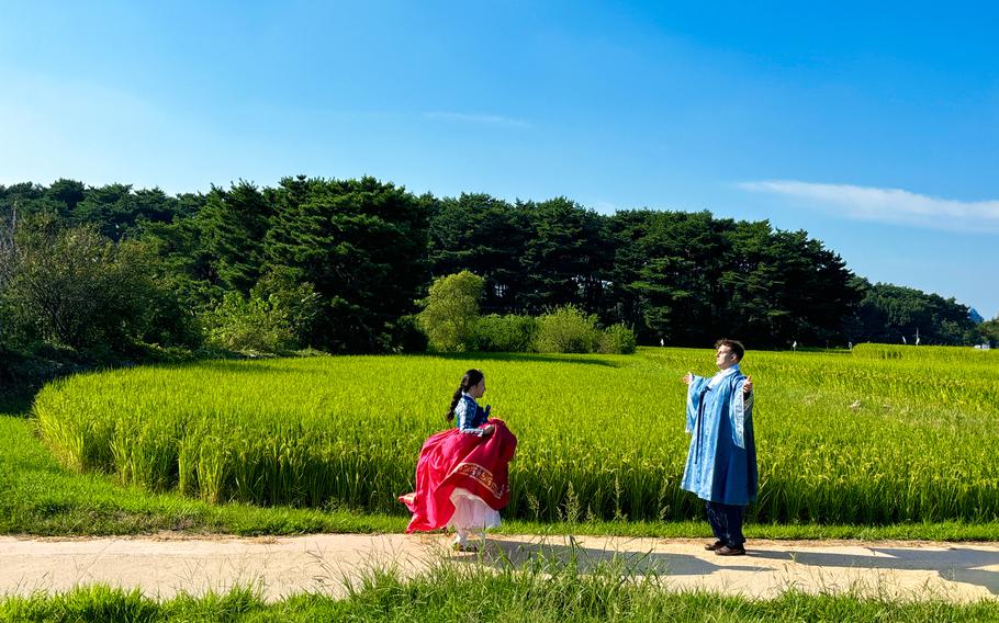 Two people with rented hanbok face each other on a path.