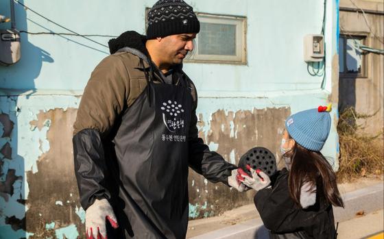 U.S. Army Staff Sgt. Miguel Bermejo, assigned to U.S. Army Garrison Yongsan-Casey Headquarters and Headquarters Company, gives a coal briquette to a child in the neighborhood of Sangpae, Dongducheon city, South Korea, Nov. 23, 2024. 