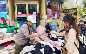 a woman is buying clothing at a booth outside.