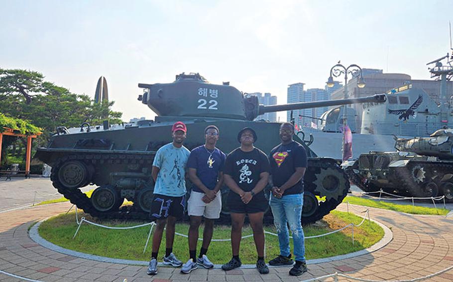 Participants pose for a photo in front of a tank.