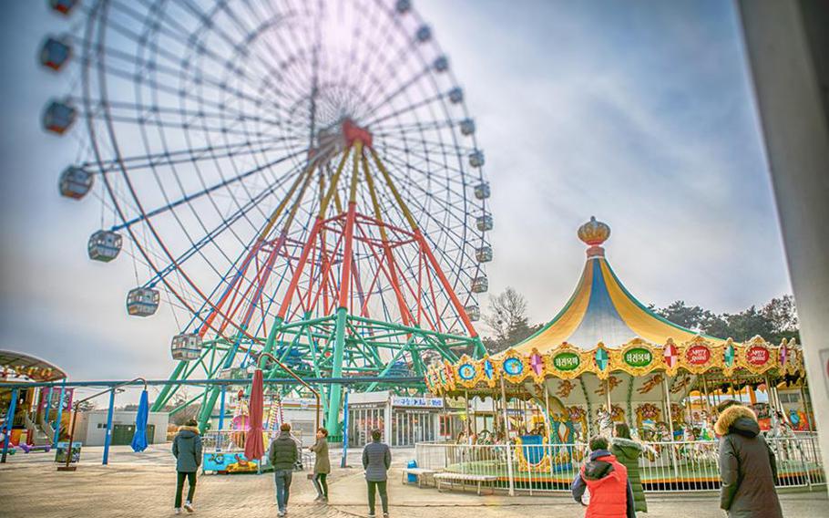 ferris wheel and merry-go-round in the theme park. some visitors are walking.