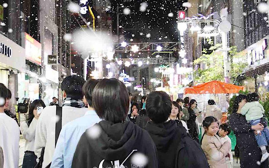 artificial snow is falling on the crowded street.