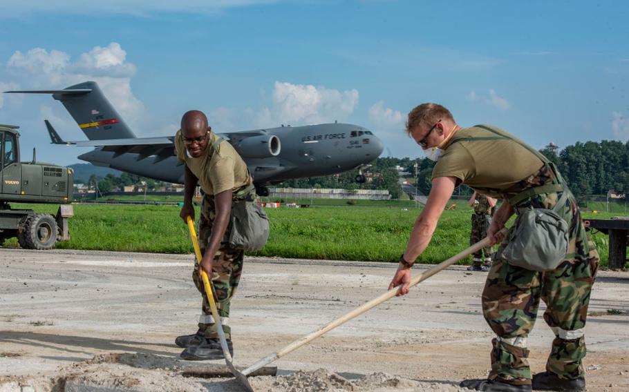 U.S. Air Force Staff Sgt. Connor Stevens, left, 51st Civil Engineer Squadron structural engineer, and Staff Sgt. Hayden Brooks, 51st CES structural engineer, conduct rapid airfield damage repair while a C-17 Globemaster III lands.